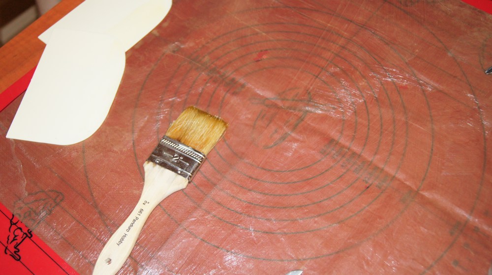 Forberedelser før du går i gang med å koke dropsmassen: Legg en håndduk under teflonmatten og smør den med smeltet smør. Smør også deigskrapene og saksen som skal brukes til å klippe dropsene.